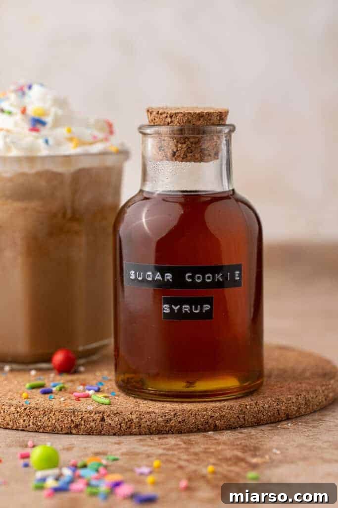 Homemade Starbucks sugar cookie syrup in a corked glass bottle with a holiday sugar cookie latte behind it