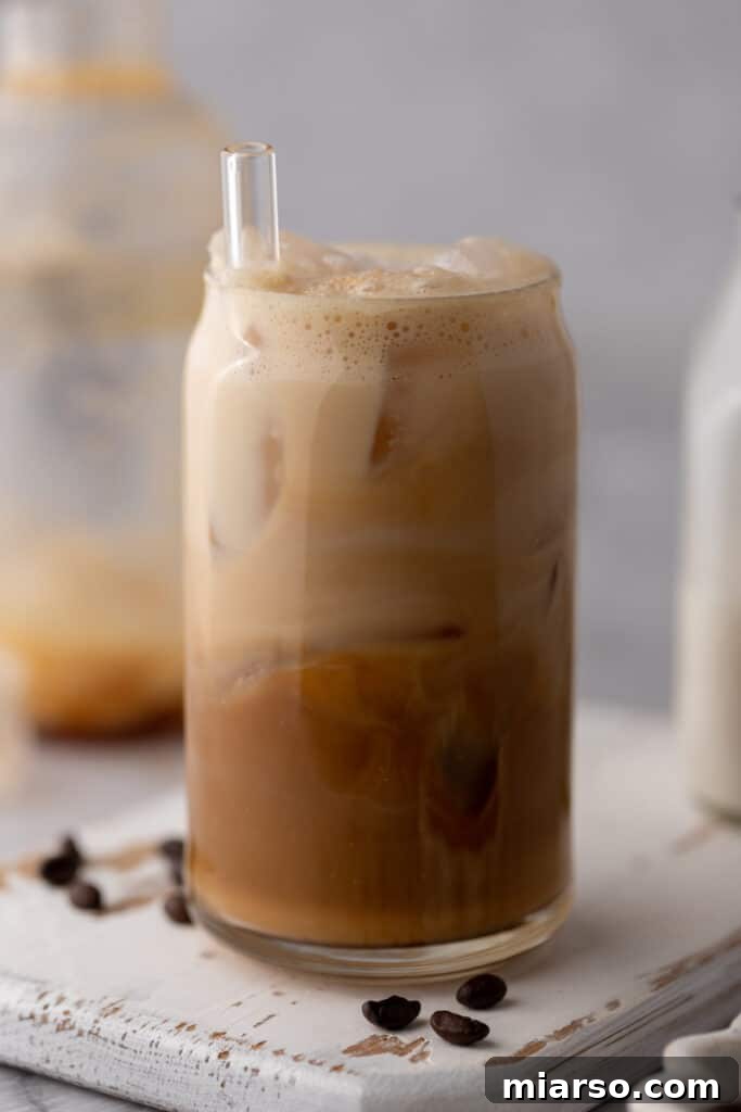 Homemade Starbucks iced caramel latte in a glass with a straw and coffee beans on the side