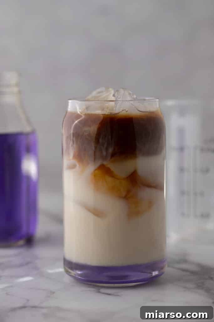 Homemade Starbucks iced lavender oatmilk latte with espresso swirling into milk with a purple lavender syrup bottle