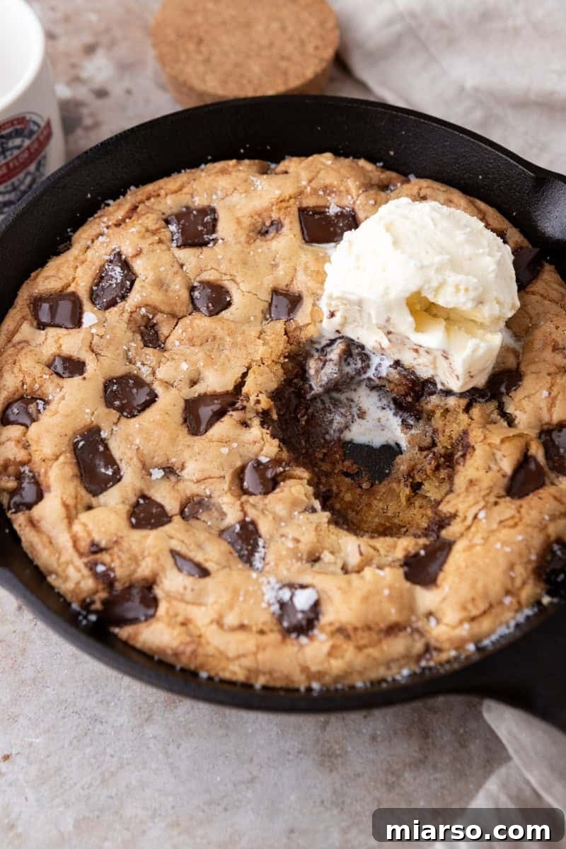 Nutty Brown Butter Chocolate Chip Skillet Cookie 2 Brown butter chocolate chip skillet cookie in an 8-inch cast iron skillet with a scoop of vanilla ice cream and flaky sea salt with a spoonful scooped out showing the gooey center