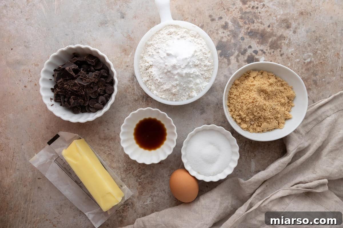 Nutty Brown Butter Chocolate Chip Skillet Cookie 3 Ingredients laid out on a counter including butter, an egg, chopped chocolate, flour, brown sugar, granulated sugar, and vanilla extract