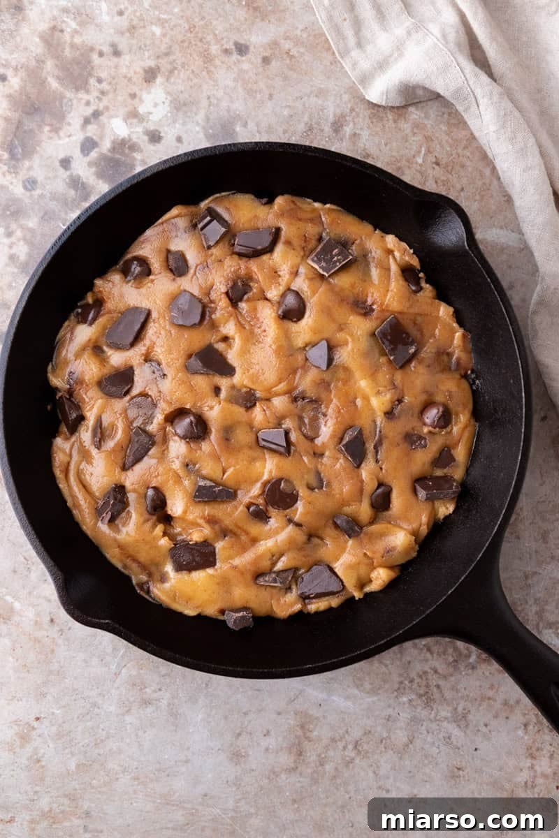 Nutty Brown Butter Chocolate Chip Skillet Cookie 8 Unbaked chocolate chip cookie dough pressed into an even layer in a greased 8-inch cast iron skillet with chocolate chunks visible on top