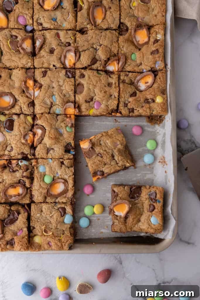 Effortless Easter Treats for Spring Gatherings 11 Cadbury egg cookie bars, perfectly sliced into squares in a parchment-lined baking pan, studded with pastel M&Ms and baked-in Cadbury creme eggs.