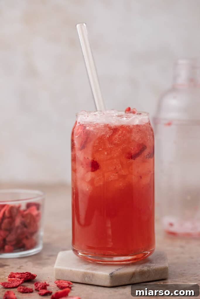 Effortless Easter Treats for Spring Gatherings 9 Homemade Starbucks Strawberry Acai Refresher in a glass can cup with a glass straw and freeze-dried strawberries on the side.