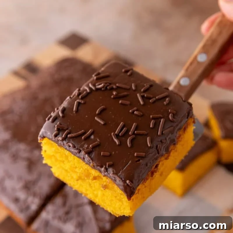 A slice of bright orange carrot cake with thick chocolate glaze and chocolate sprinkles being lifted with a wooden-handled knife