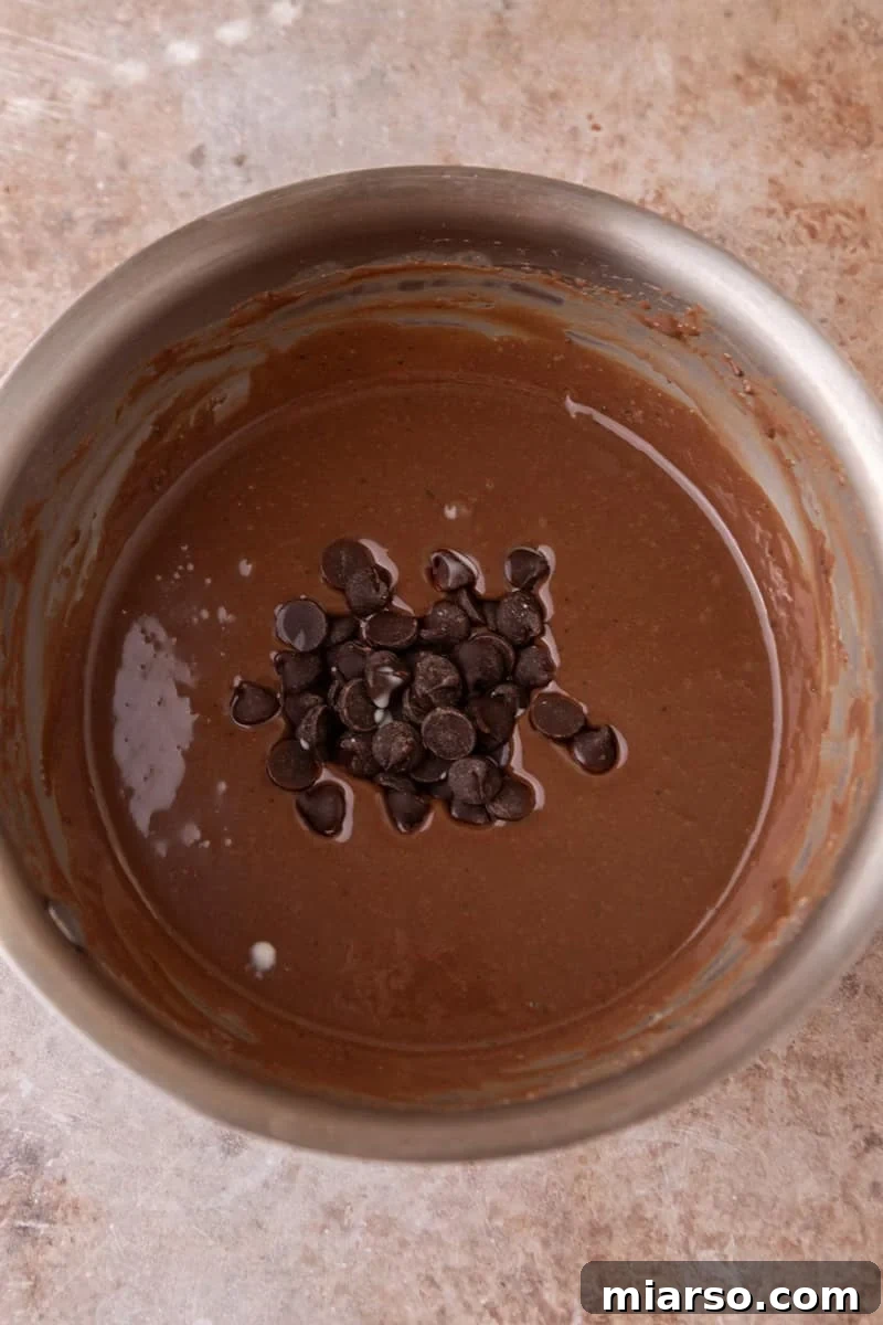 Dark chocolate chips added to the warm chocolate glaze in a saucepan ready to be stirred in