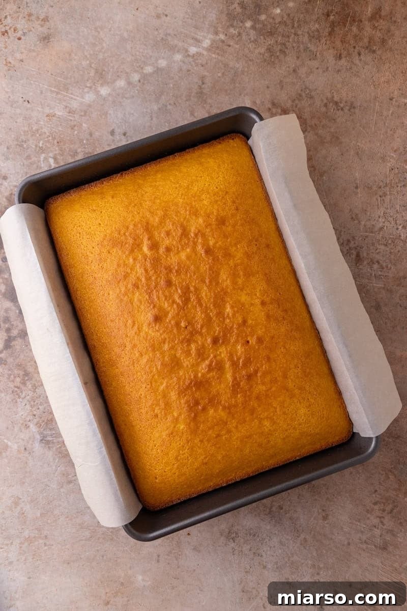 A freshly baked golden orange cake cooling in a parchment-lined 9x13 pan