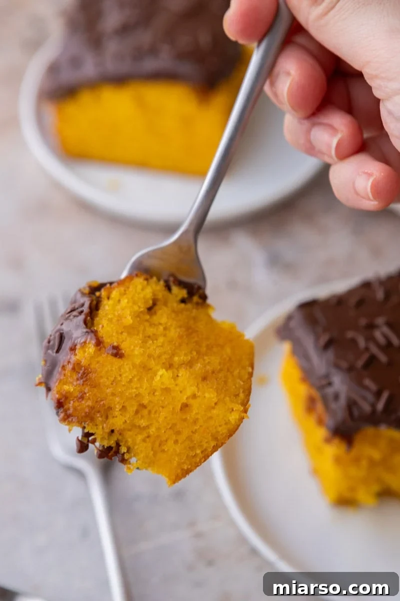 A fork holding a bite of orange cake with chocolate glaze showing the soft moist crumb up close