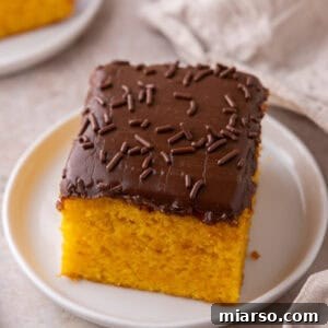 A single square of carrot cake with chocolate frosting and sprinkles on a small white plate