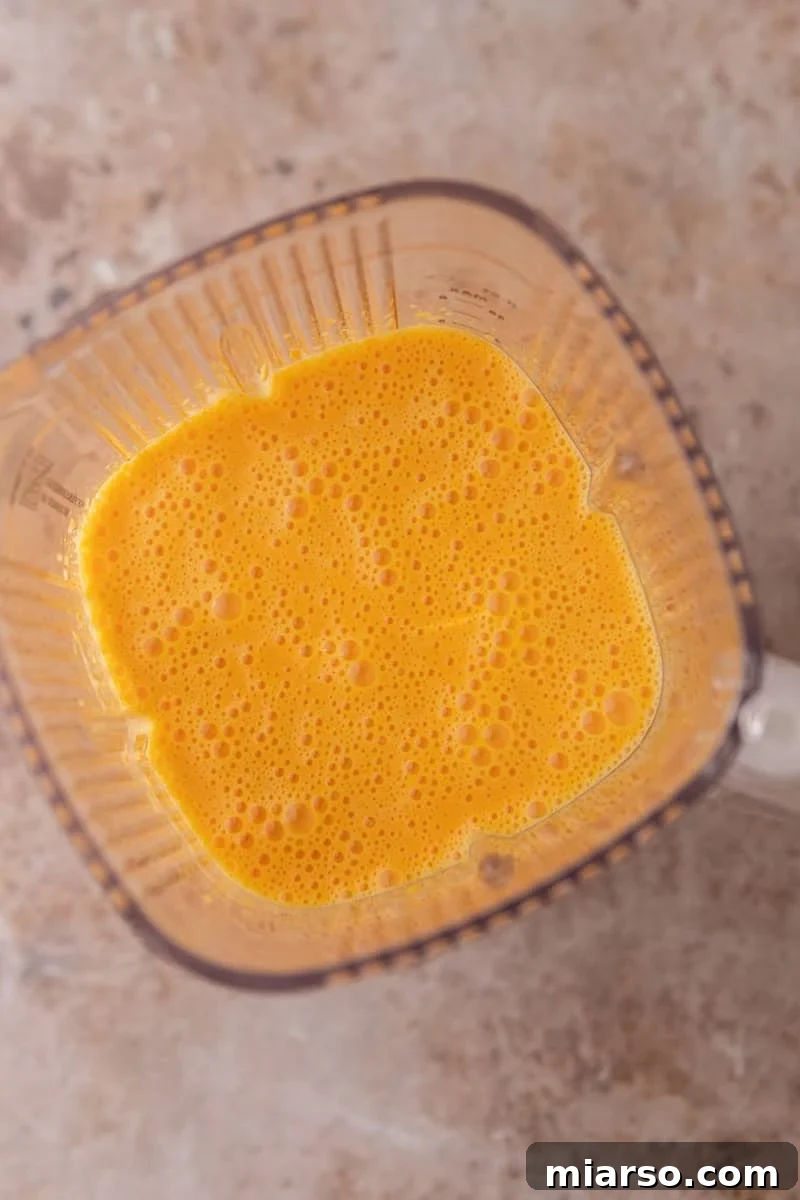 Bright orange blended batter in a blender viewed from above with small air bubbles on the surface