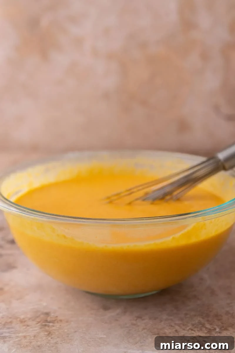 Smooth orange cake batter in a glass mixing bowl with a whisk resting inside
