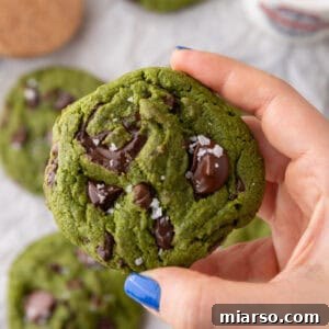 Velvet Matcha Chocolate Chip Cookies 13 Hand holding a thick green matcha cookie with melty chocolate chunks and flaky sea salt on top