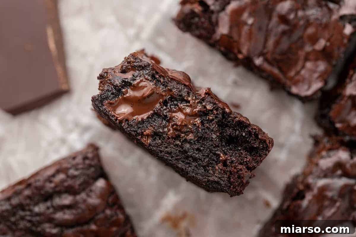 A single small batch brownie, boasting a melted chocolate chunk center, artfully placed on parchment paper to highlight its ultra-fudgy interior texture.