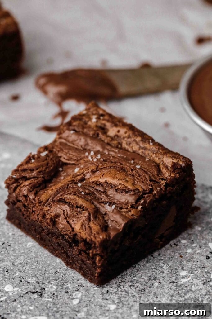 A perfectly portioned small batch Nutella brownie square, featuring enticing swirls of Nutella on top and a rich, fudgy chocolate interior, elegantly sprinkled with flaky sea salt.