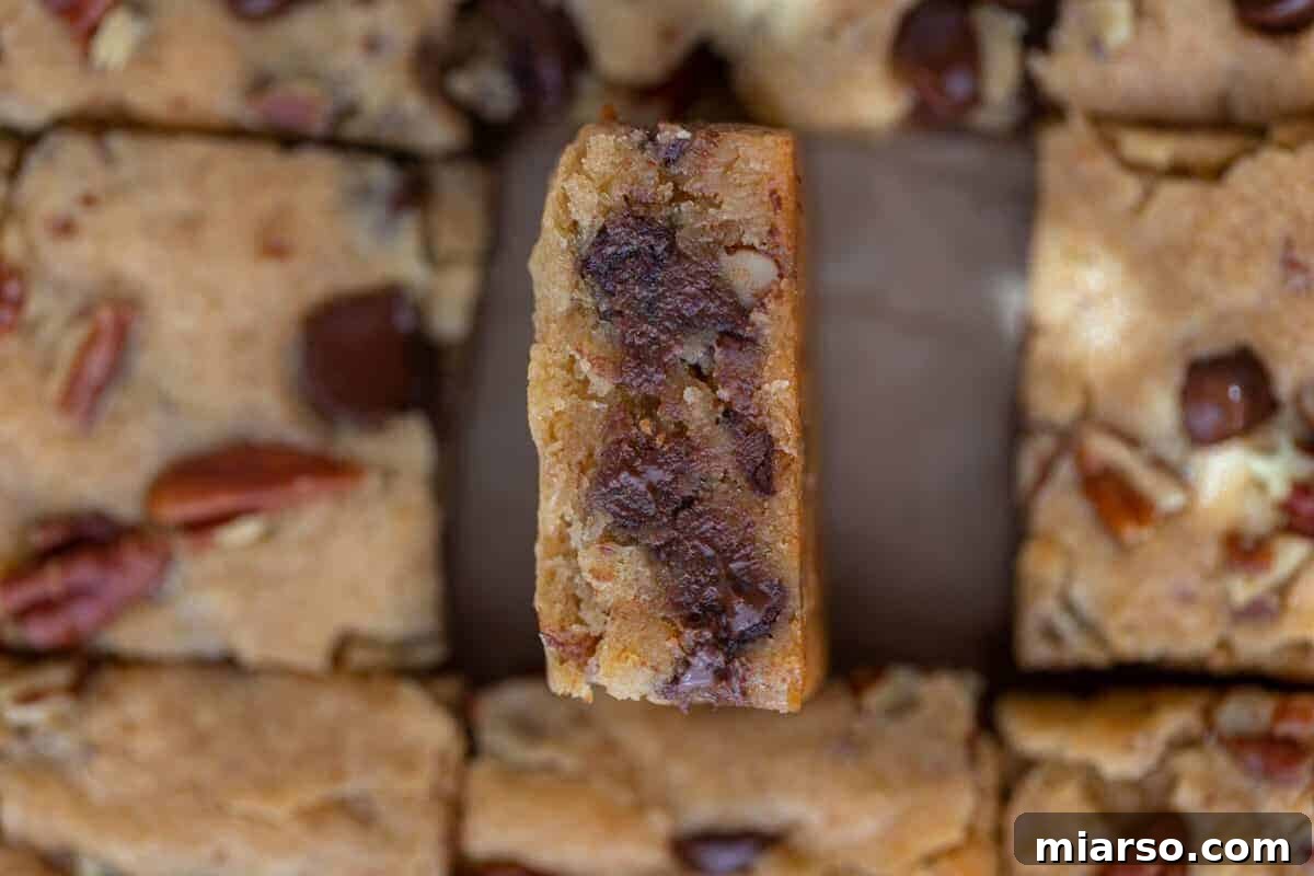 Chewy pecan chocolate chip blondies, expertly sliced into bars, with one piece tilted to display its fudgy interior, generously studded with melted chocolate and crunchy pecans.
