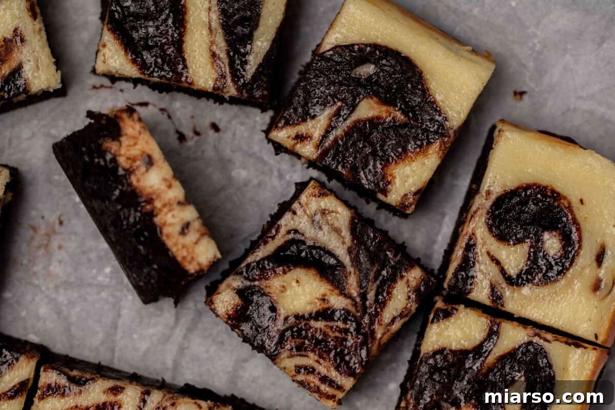 Exquisite cream cheese cheesecake brownies, perfectly sliced into squares, showcasing a beautiful marbled swirl pattern of tangy cream cheese and rich fudgy chocolate brownie, with one piece tilted on its side for emphasis.