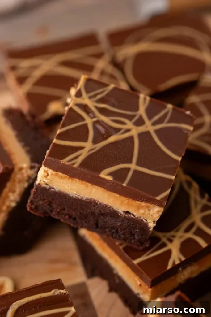 Buckeye brownies showcasing three distinct, irresistible layers: a rich fudgy brownie base, a smooth peanut butter filling, and a glossy chocolate ganache finish, beautifully adorned with a delicate peanut butter drizzle on top.