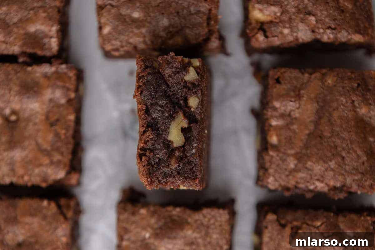 Decadent fudge walnut brownies, perfectly sliced into squares, with one piece tilted to display its dense chocolate interior generously studded with chopped walnut pieces.