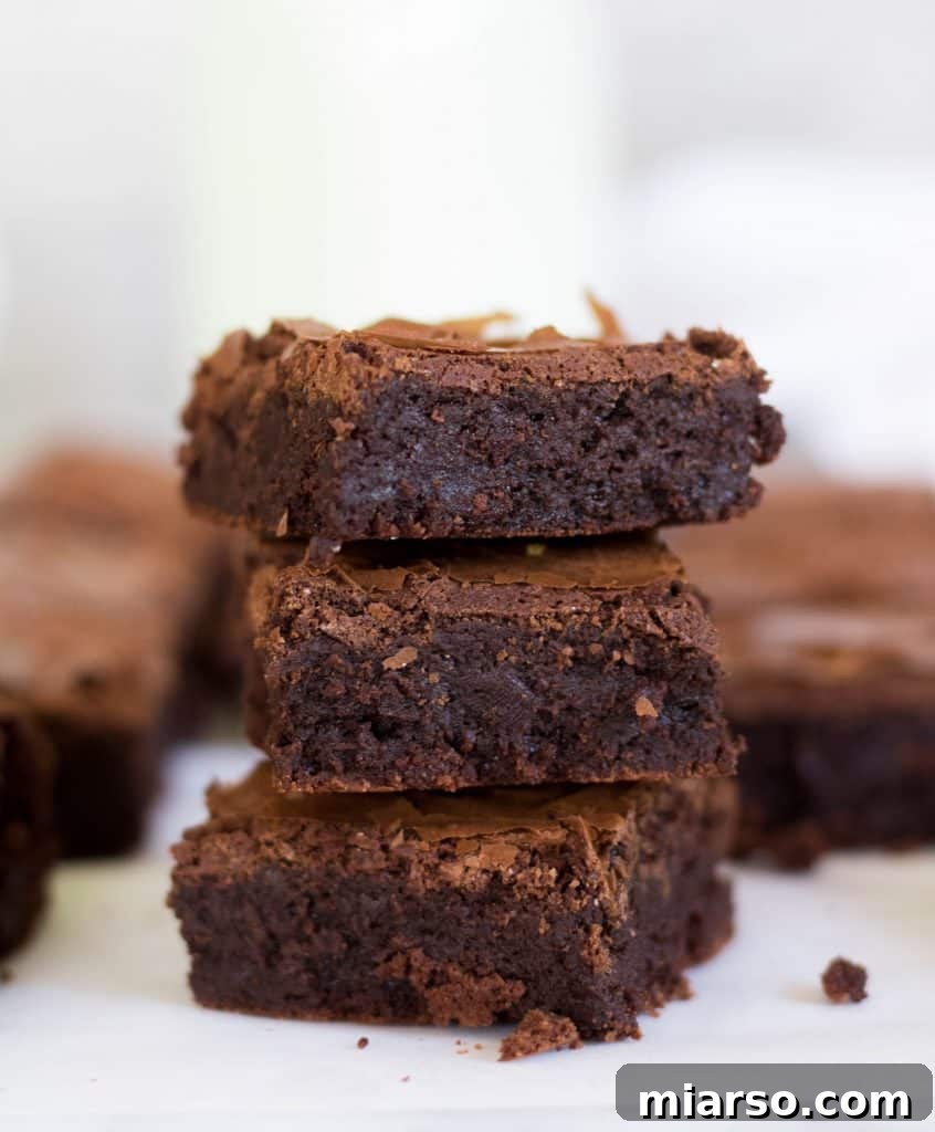 Stack of three bakery-style brownies without cocoa powder, showcasing their ultra-fudgy, dense interior and delicate, thin crinkly crust.