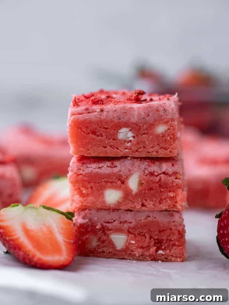 Vibrant pink strawberry cake mix brownies, perfectly sliced into squares, with one piece tilted to reveal its fudgy, bright pink interior dotted with melted white chocolate chips.