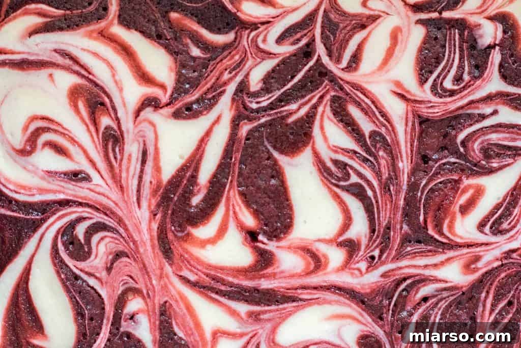Close-up overhead view of exquisite cheesecake swirled red velvet brownies, showcasing the beautiful marbled pattern created by the tangy cream cheese and vibrant red velvet brownie batter.