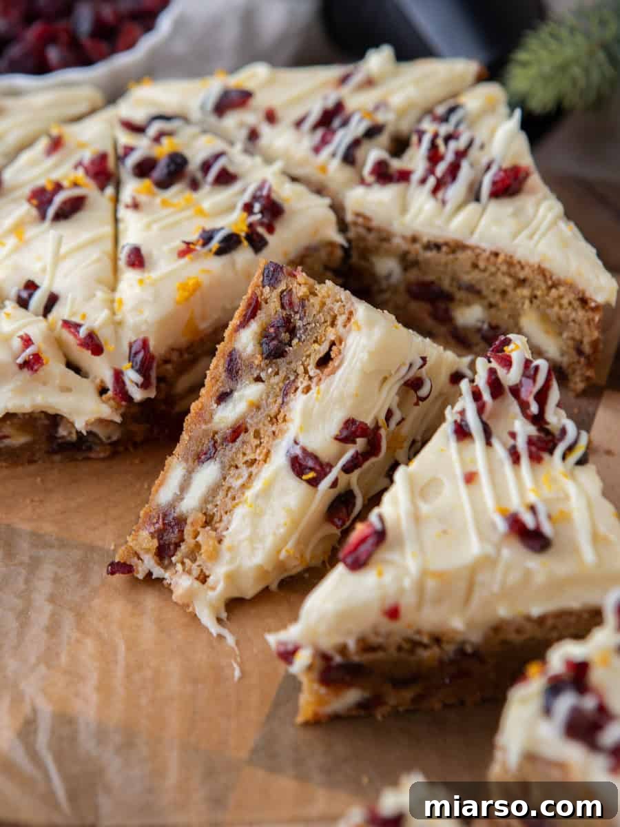 Exquisite copycat Starbucks cranberry bliss bars, perfectly sliced into triangles on parchment paper, revealing their chewy blondie base adorned with creamy cream cheese frosting, sweet dried cranberries, and zesty orange zest on top.