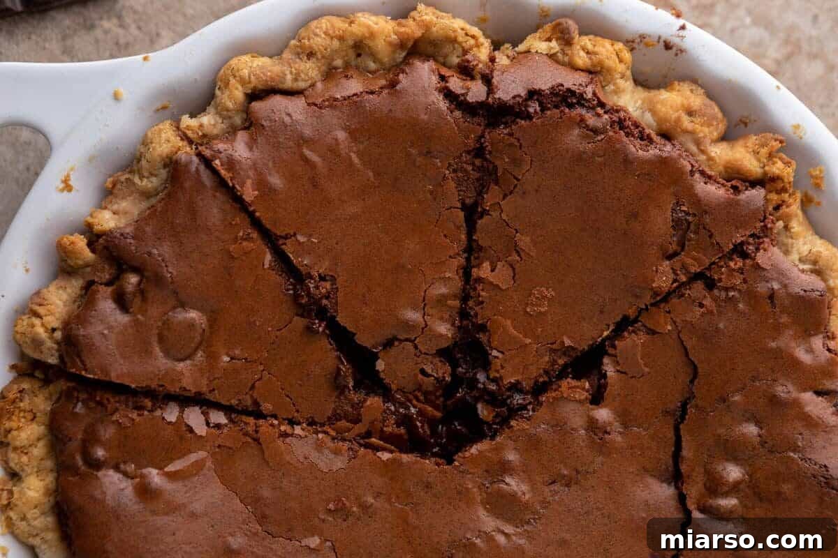 Overhead view of a luscious brownie pie in a white pie dish, featuring a golden, flaky pie crust and a rich fudgy chocolate brownie filling, perfectly sliced into triangular pieces.