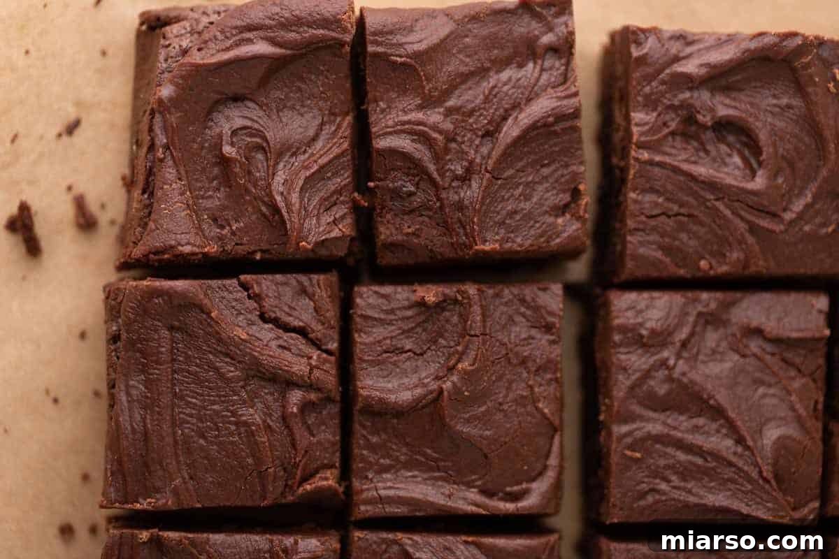 Rich brownies topped with thick, swirled chocolate brownie frosting, perfectly sliced into squares on parchment paper, showcasing the luxurious fudgy frosting layer.