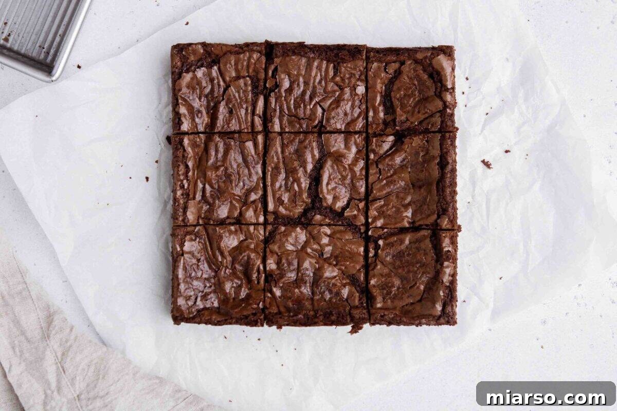 Overhead shot of upgraded boxed brownies, perfectly sliced into nine squares on parchment paper, showcasing their shiny, crinkly tops and impressively fudgy texture.
