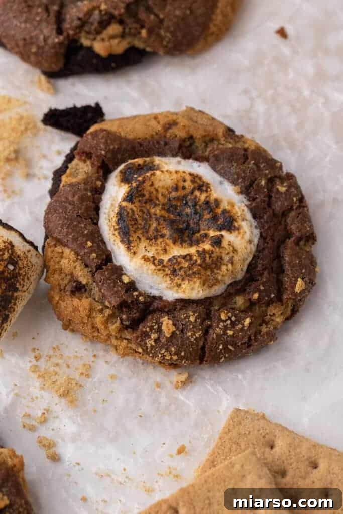 An irresistible Crumbl s'mores brownie cookie on parchment paper, showcasing its expertly layered chocolate brownie cookie base, adorned with graham cracker crumbs and a perfectly toasted marshmallow on top.