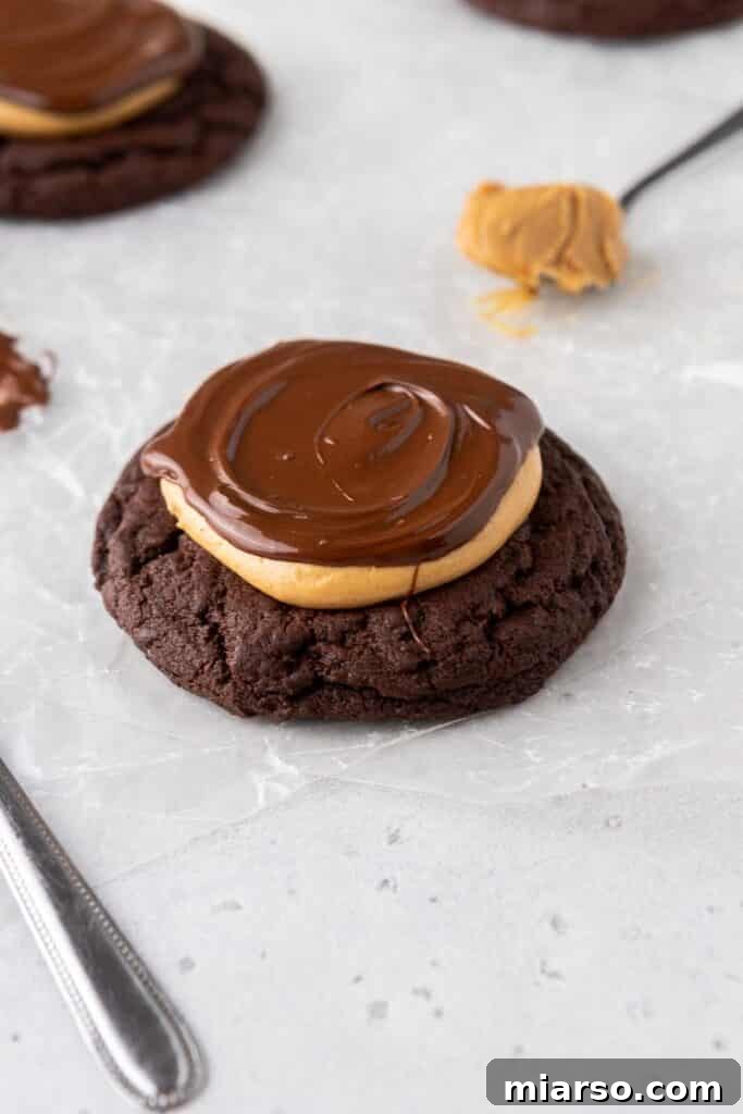 A rich Crumbl peanut butter brownie cookie on parchment paper, featuring a thick chocolate brownie cookie base topped with creamy peanut butter and a glossy chocolate ganache drizzle.