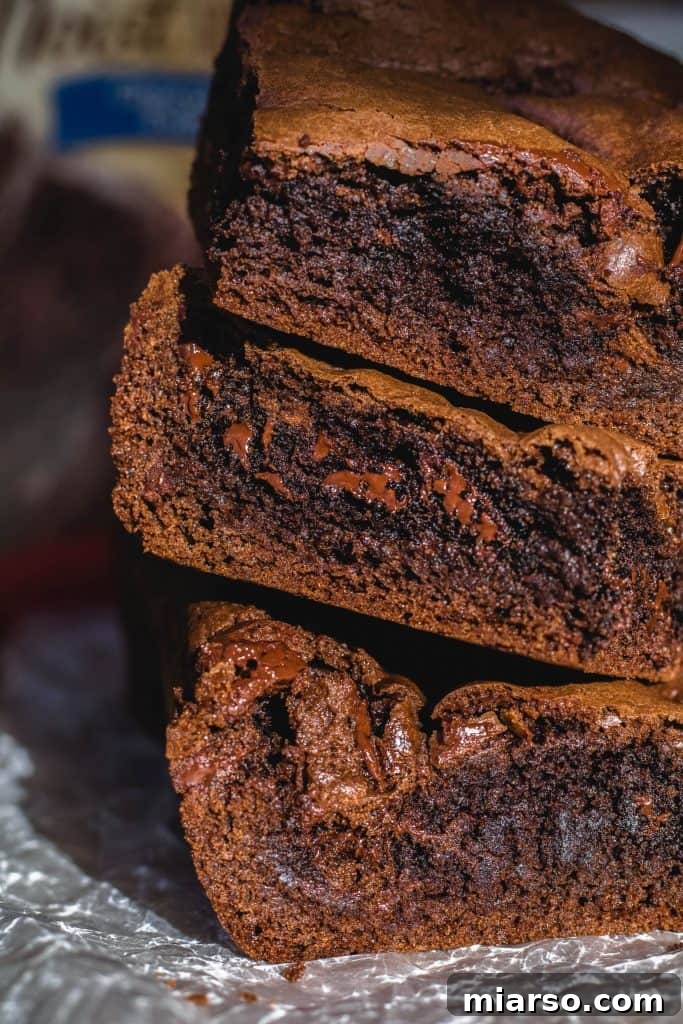 Close-up stack of decadent cake mix brownies, revealing tantalizing melted chocolate pools and an irresistibly dense, chewy interior.