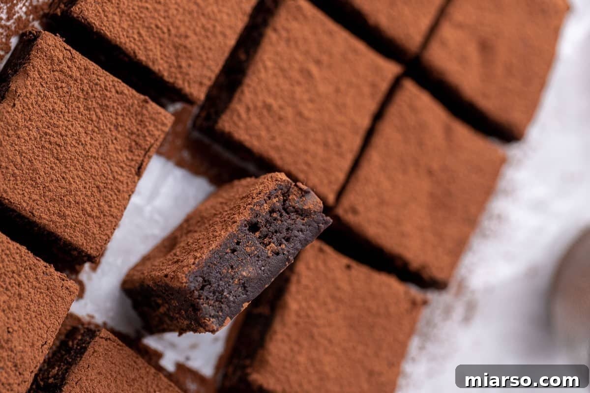 Decadent red wine brownies, elegantly dusted with cocoa powder and sliced into perfect squares, with one piece tilted to highlight its dense, fudgy chocolate center.