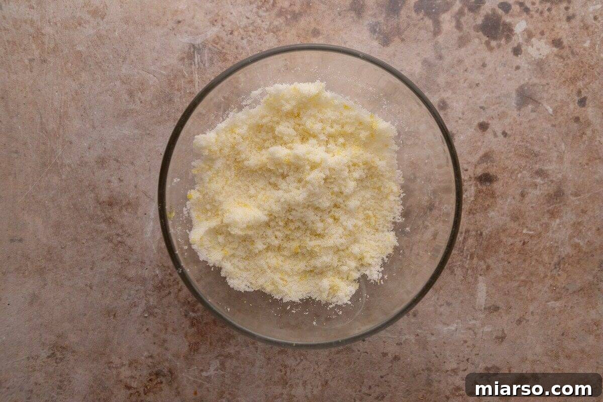 Lemon zest rubbed into granulated sugar in a glass bowl for lemon roll filling