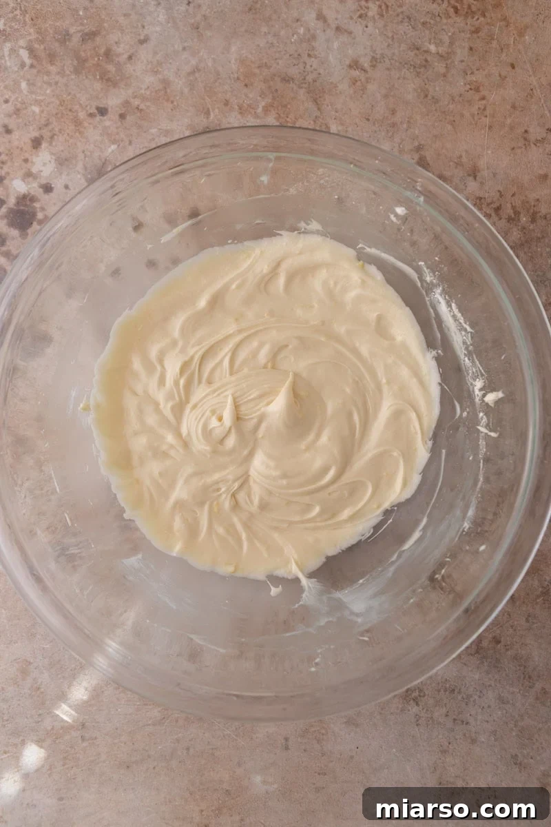 Smooth creamy lemon cream cheese frosting in a glass bowl ready to spread on lemon rolls