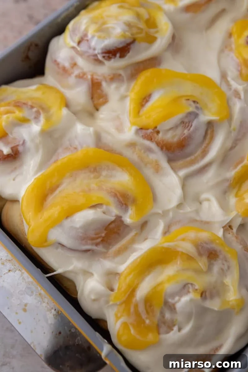 Pan of lemon rolls covered in cream cheese frosting with lemon curd swooped on top of each roll