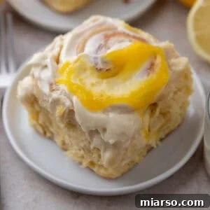 A single lemon roll with lemon curd on a small white plate with lemons in the background