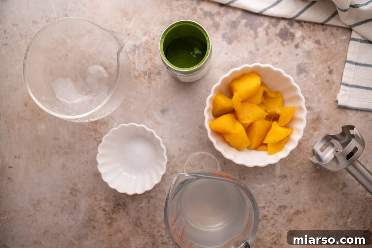 ingredients for mango matcha drink with fresh mango chunks coconut water and immersion blender