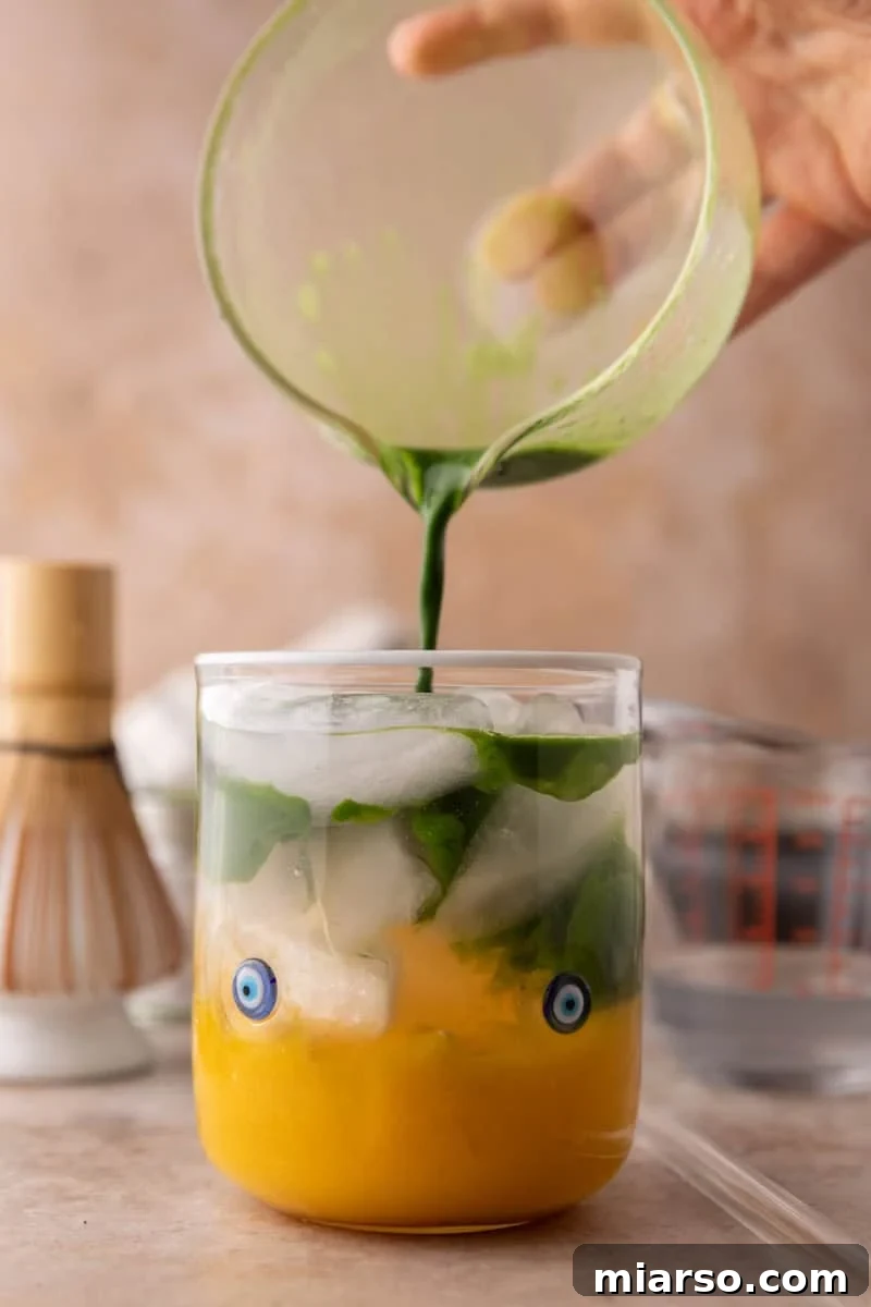 pouring whisked matcha into mango matcha drink creating a layered marble effect
