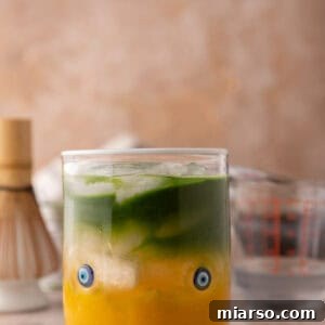 iced mango matcha drink with coconut water in a glass with golden mango and green matcha layers