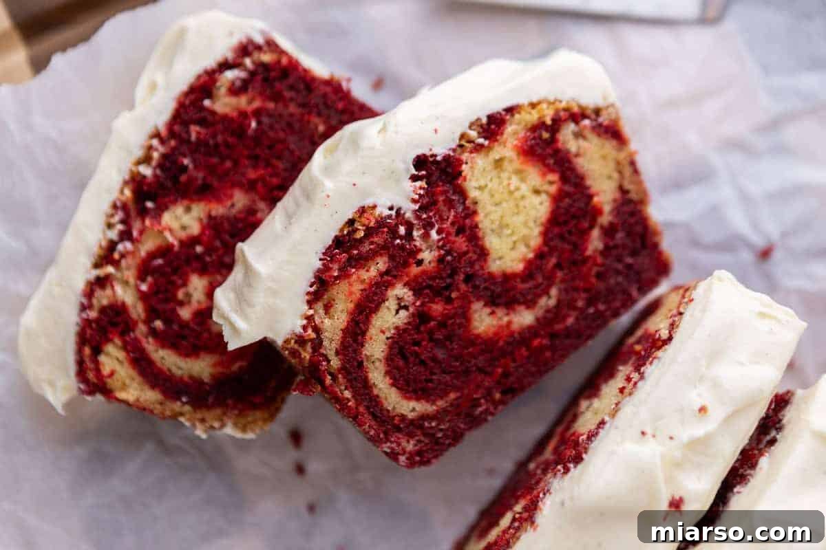 A perfectly sliced Red Velvet Marble Loaf Cake revealing distinct swirls of red velvet and vanilla cake, generously topped with thick, white cream cheese frosting.