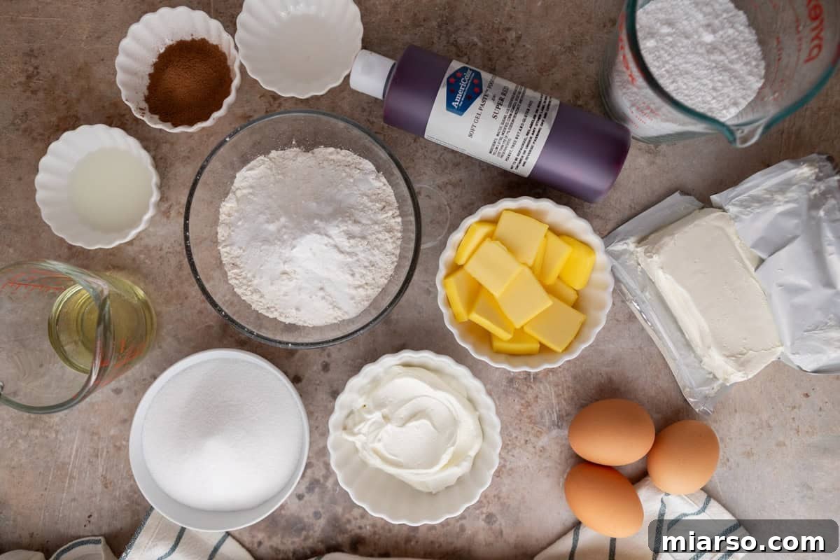 Various baking ingredients meticulously arranged in bowls on a white surface, including all-purpose flour, butter, sour cream, eggs, granulated sugar, cocoa powder, and cream cheese for the frosting, highlighting the quality of components.