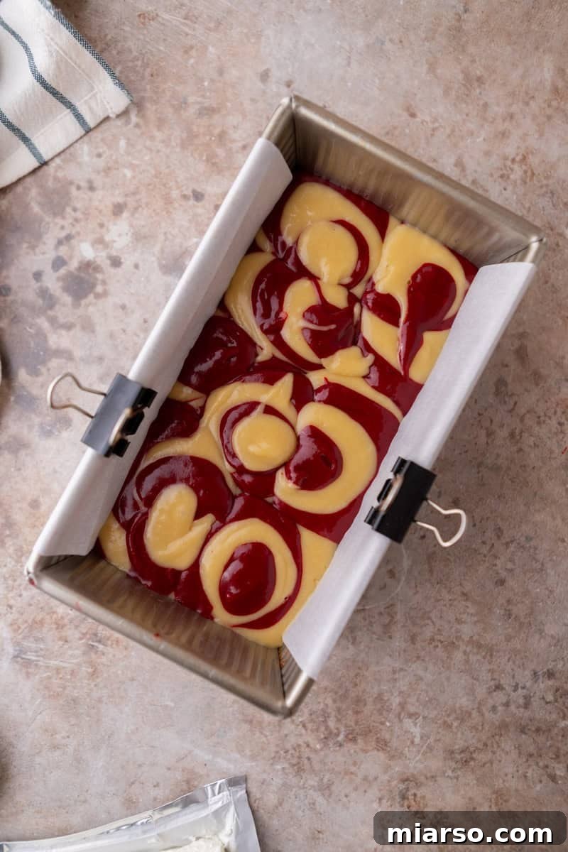 An overhead view of distinct vanilla and red velvet cake batters carefully dolloped into a parchment-lined loaf pan, ready for the gentle swirling process to create a beautiful marble effect.