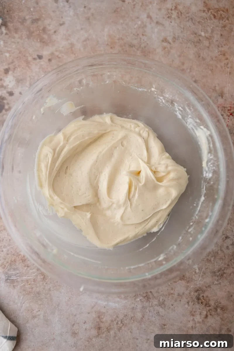 An overhead shot of velvety cream cheese frosting, perfectly whipped and ready to be spread, showcasing visible flecks of vanilla bean for added depth of flavor.