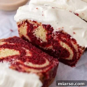 Thick slices of marble loaf cake with red velvet and vanilla swirls topped with cream cheese frosting.