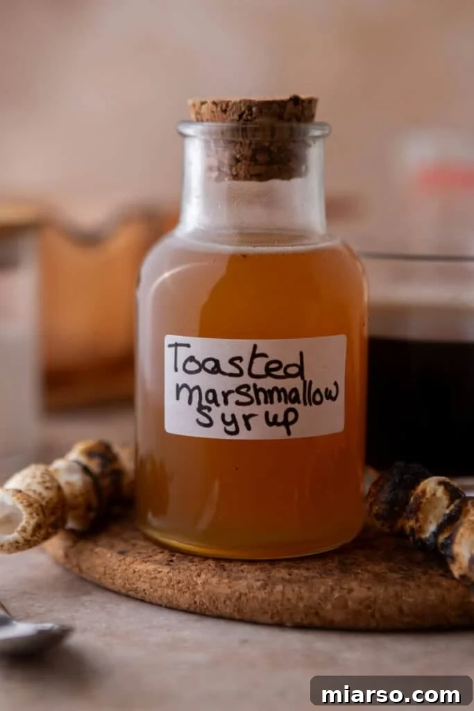 A charming glass bottle with a cork stopper, showcasing golden homemade toasted marshmallow syrup.