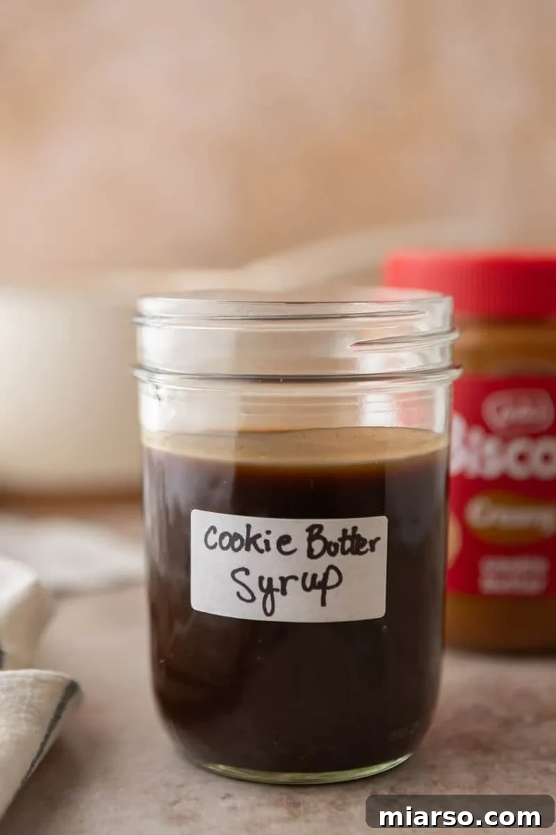 Biscoff Cookie Butter Latte Syrup 2 Homemade cookie butter coffee syrup in a labeled mason jar with a jar of Lotus Biscoff cookie butter in the background.