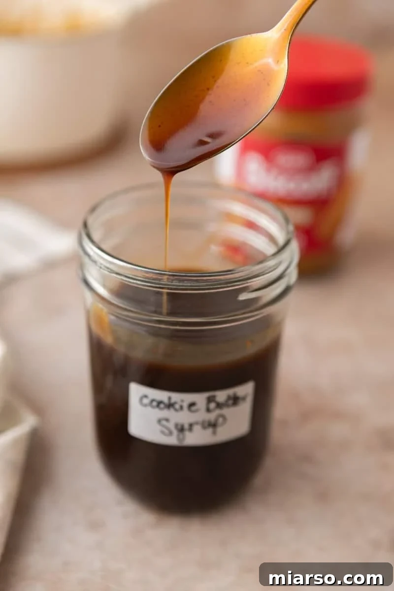 Biscoff Cookie Butter Latte Syrup 6 A spoon drizzling homemade cookie butter syrup into a labeled mason jar showing the thick, pourable consistency.