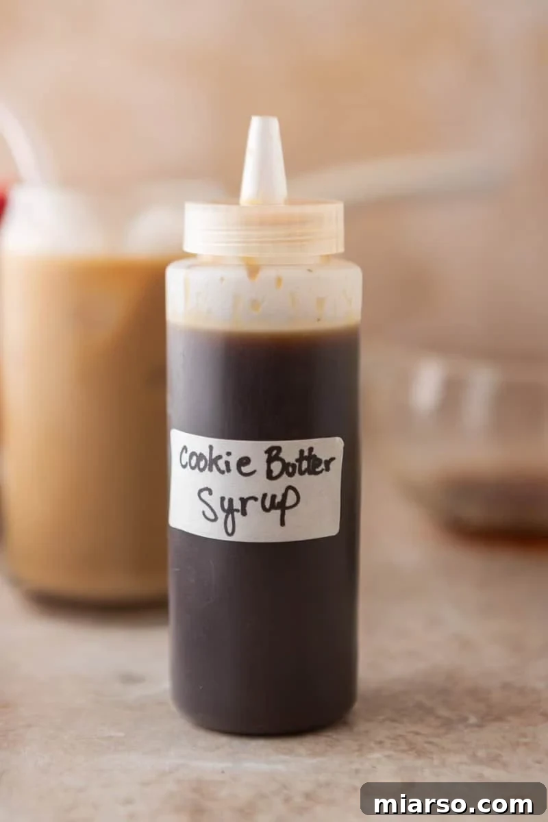 Biscoff Cookie Butter Latte Syrup 7 Homemade cookie butter coffee syrup in a squeeze bottle with a cookie butter iced latte in the background.