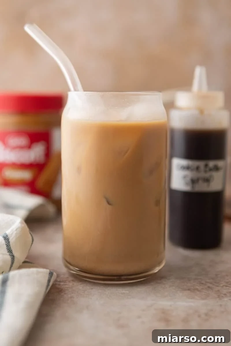 Biscoff Cookie Butter Latte Syrup 8 A cookie butter iced latte made with homemade Biscoff syrup in a glass with a straw, with the syrup bottle and Biscoff jar in the background.